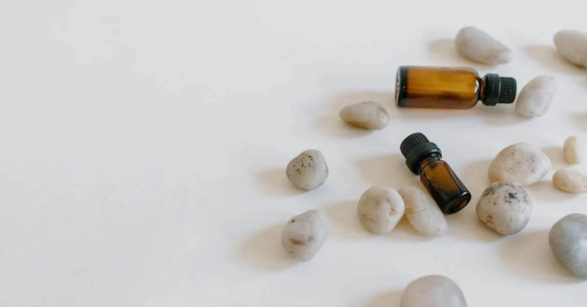 Two amber bottles of essential oils surrounded by small stones on a white surface.